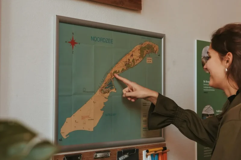 vrouw-wijst-op-kaart-van-vlieland-aan-de-muur-in-donia-huys.